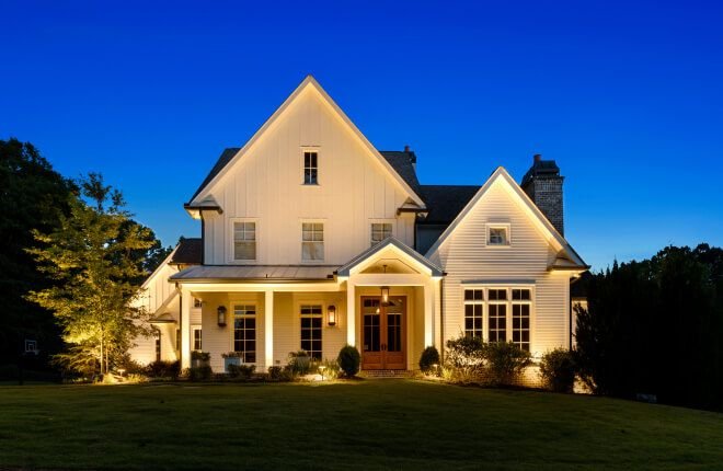 Two-story farmhouse with warm white roofline lights at dusk